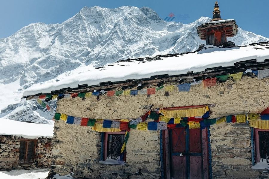 Traditional Tibetan monastery with colorful prayer flags against snow-covered Himalayan mountains